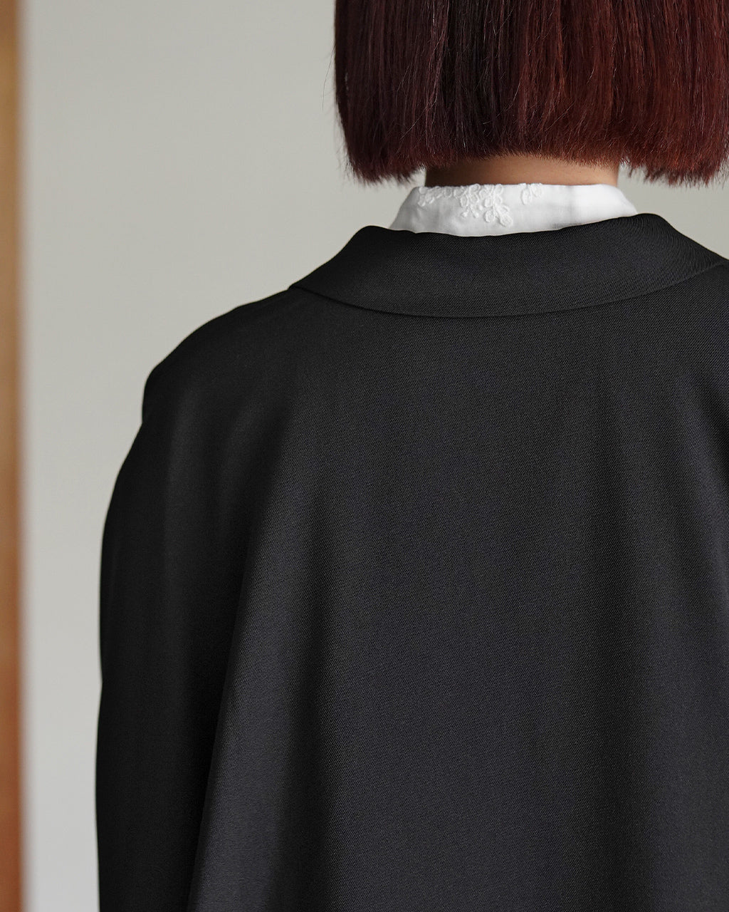 後ろ姿のジャケット風シャツ。黒色の生地に白い襟が覗き、長めの丈と柔らかなドレープが印象的です。