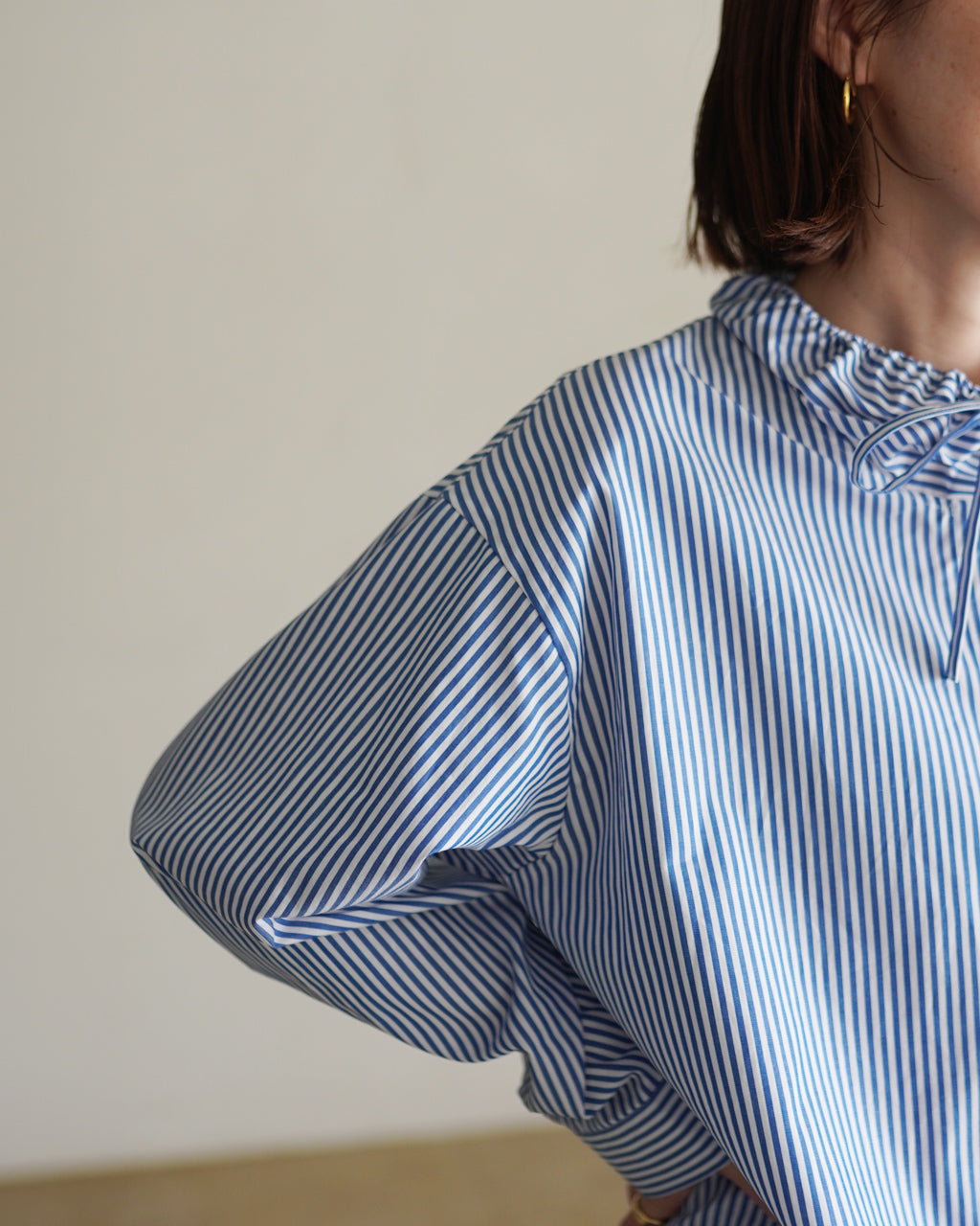 mizuiro ind の青×白ストライプ柄シャツ、首元のギャザーとボリューム袖が特徴的なディテールショット。近接の縦ストライプと袖口のフォルムが分かる着用イメージ。