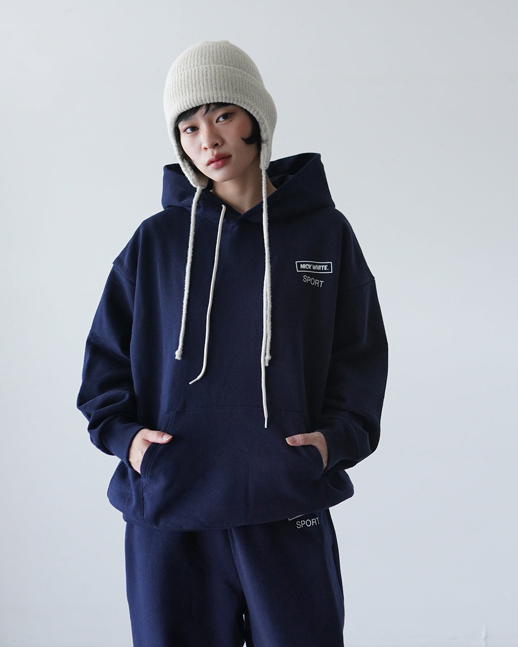 フード付きスウェットシャツの正面ショット。ネイビーの本体と白のドローコード、胸元に小さめのロゴが施されているカジュアルなデザイン。