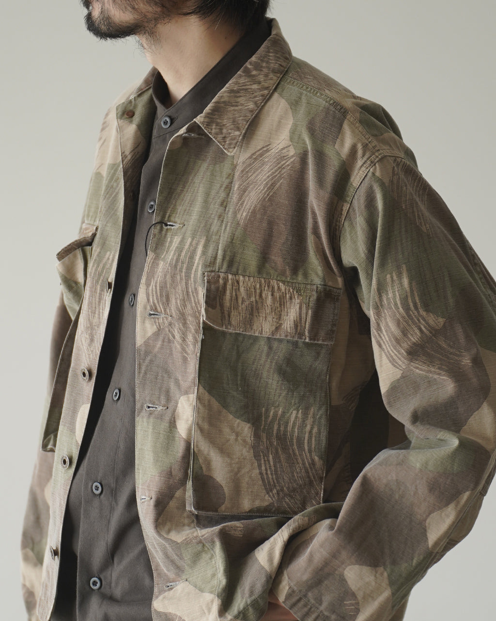 Nigel CabournのFIELD JACKET FADE CAMOの正面アップ。迷彩柄のジャケットで、前面ポケットとボタン留めが見える。