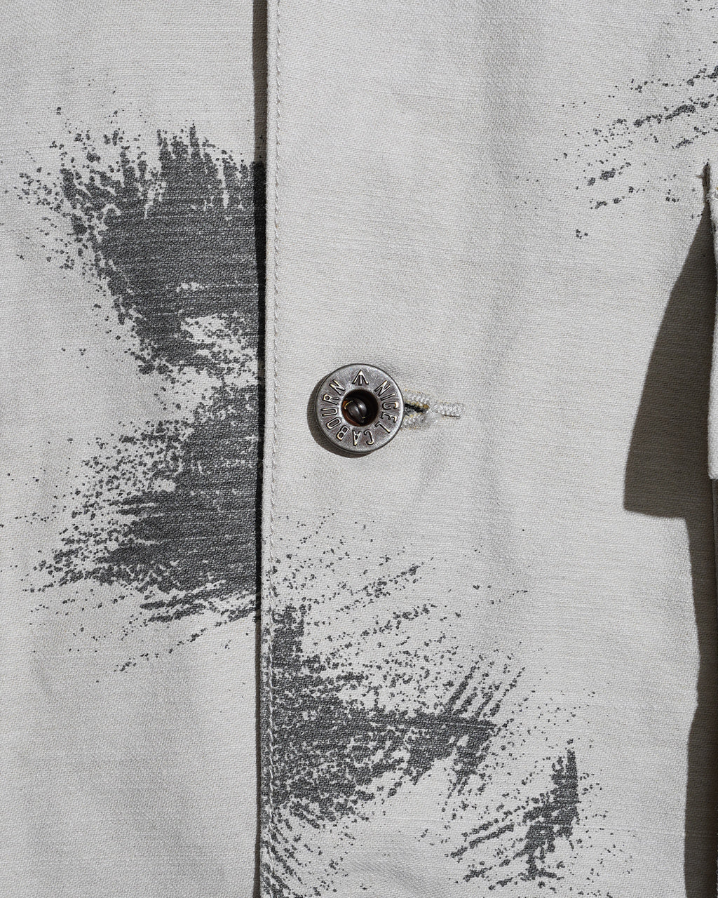 FIELD JACKET FADE CAMOの前立て部分とボタンのアップ。淡いベージュ系の素材に迷彩柄のプリントが施され、ツイル地の質感が分かるアップショットです。
