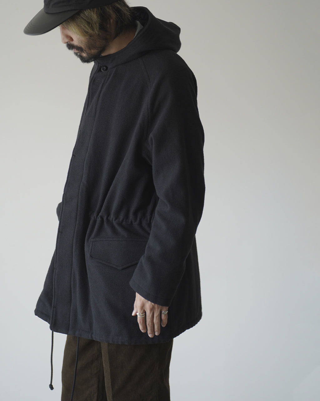 黒いフード付きジップアップコートのMANTEAU ASSAT。肩周りと裾にドローコードがあり、左胸ポケットと腰位置の大型ポケットが特徴的。