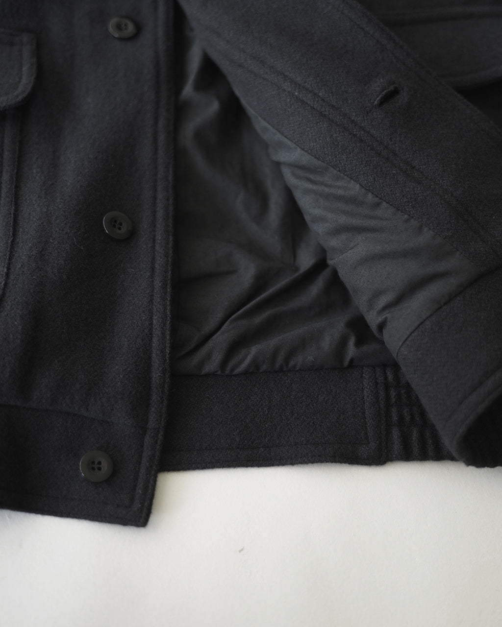 前身頃を映すブラックのVESTE ABOS。ウール100%の生地感と比翼仕立て、前部ポケットのディテールがやや光沢を抑えた質感で際立つアップショット。
