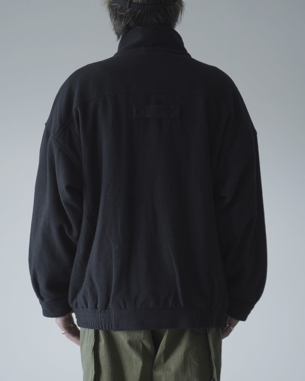背面から見た黒系のVESTE ABOS。ゆったりとしたシルエットで、裾は絞られ、襟元は立ち上がるスタンドカラー。肩回りの落ち感と腰周りのリブが特徴的。