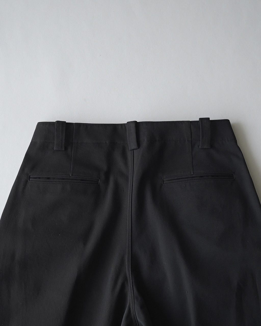 黒のパンツ後ろ姿。ベルトループと二つの後ろポケットが見える、縦縫いと股上の深さが特徴的なパンツのバックショット