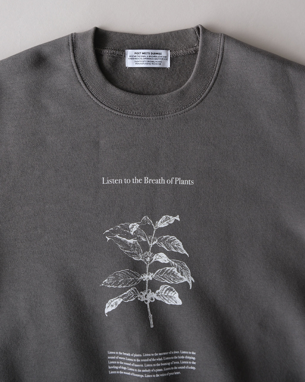 前面に大きくプリントされた植物モチーフのグラフィックと「Listen to the Breath of Plants」の文字が特徴のグレーのスウェット。