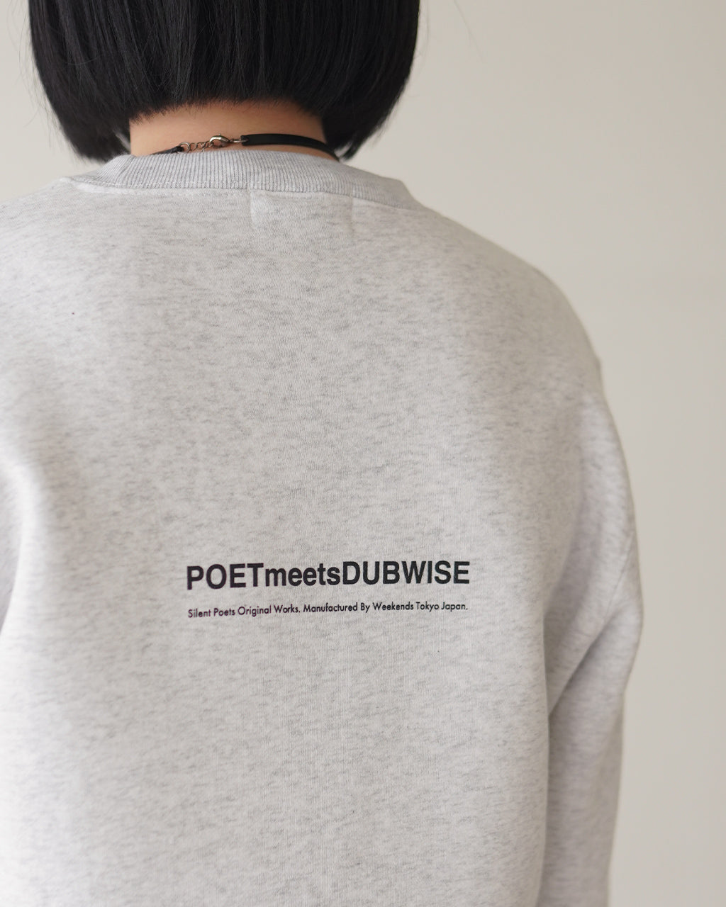 背面にPOETMeetsDUBWISEのロゴが入ったグレーのスウェット。ねじれたマチ素材と裾近くのプリントが目立たず、シンプルな雰囲気で肩幅に余裕のあるリラックスシルエット。