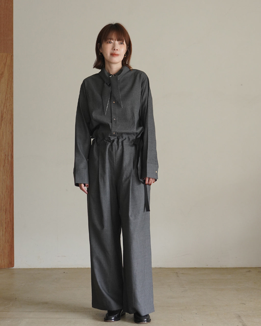 グレー系のFine Worsted Jumpsuitをモデル着用。シャツ風トップスとボリュームのあるワイドパンツの組み合わせで、前方に垂らした襟が特徴的なデザインを正面から捉えた写真。