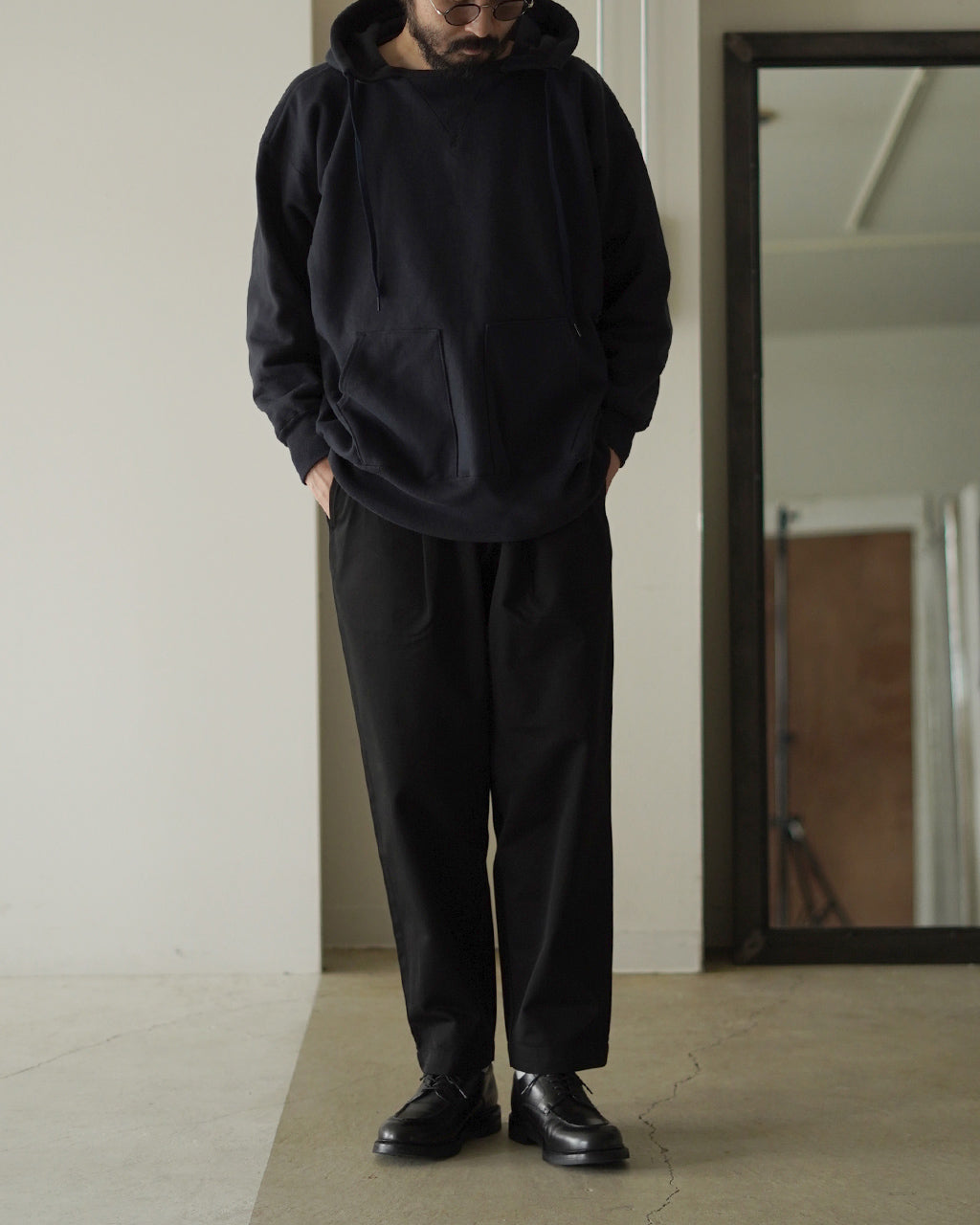 黒いフーディーとパンツのコーディネート。ゆったりとした上半身と裾に向かって細くなるシルエットが特徴的な大人のリラックススタイル。