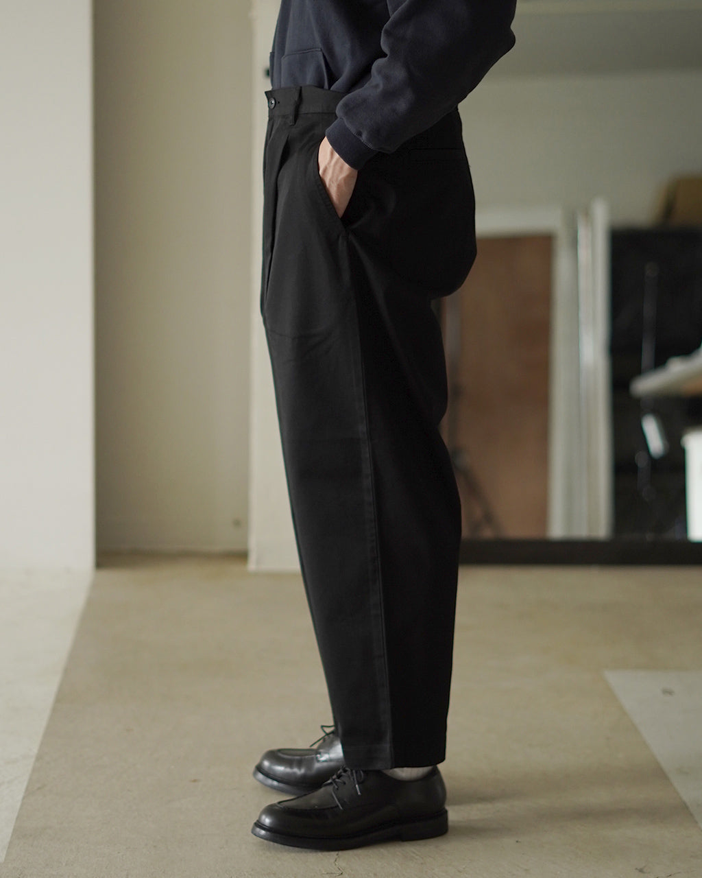 PORTER CLASSICのDuke Ellington Chinosの側面。腰回りにゆとりがあり裾に向かってすっきりと細くなるブラックのチノパンを着用したモデルの横姿。