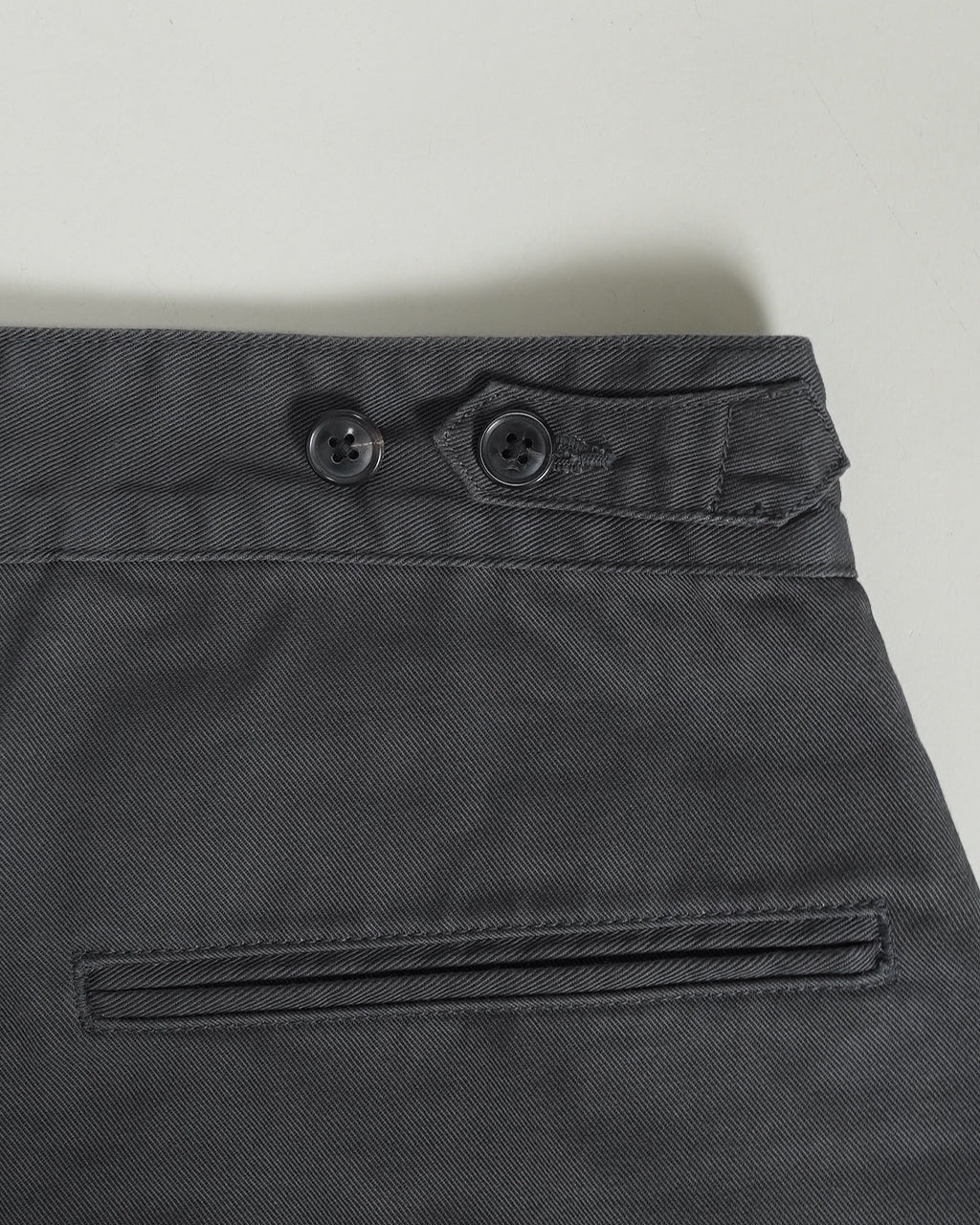 PORTER CLASSICのGENE KELLY CHINOSの裏地付きポケットと前後の細部が写るグレー系チノパンのウエスト周りアップ。ボタンとベルト留めのディテールが見えるショット。