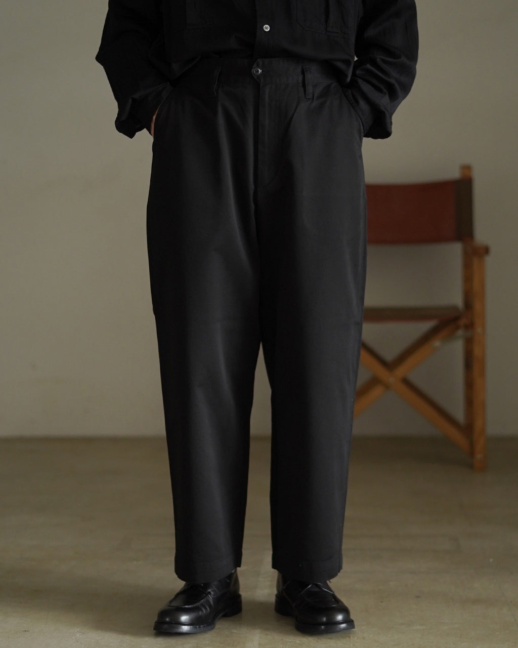 PORTER CLASSIC GENEKELLY CHINOS の正面全身画像。黒系のパンツとシャツの組み合わせで、ゆったりとした腰回りから裾に向けてややテーパードの効いたシルエットが分かる。