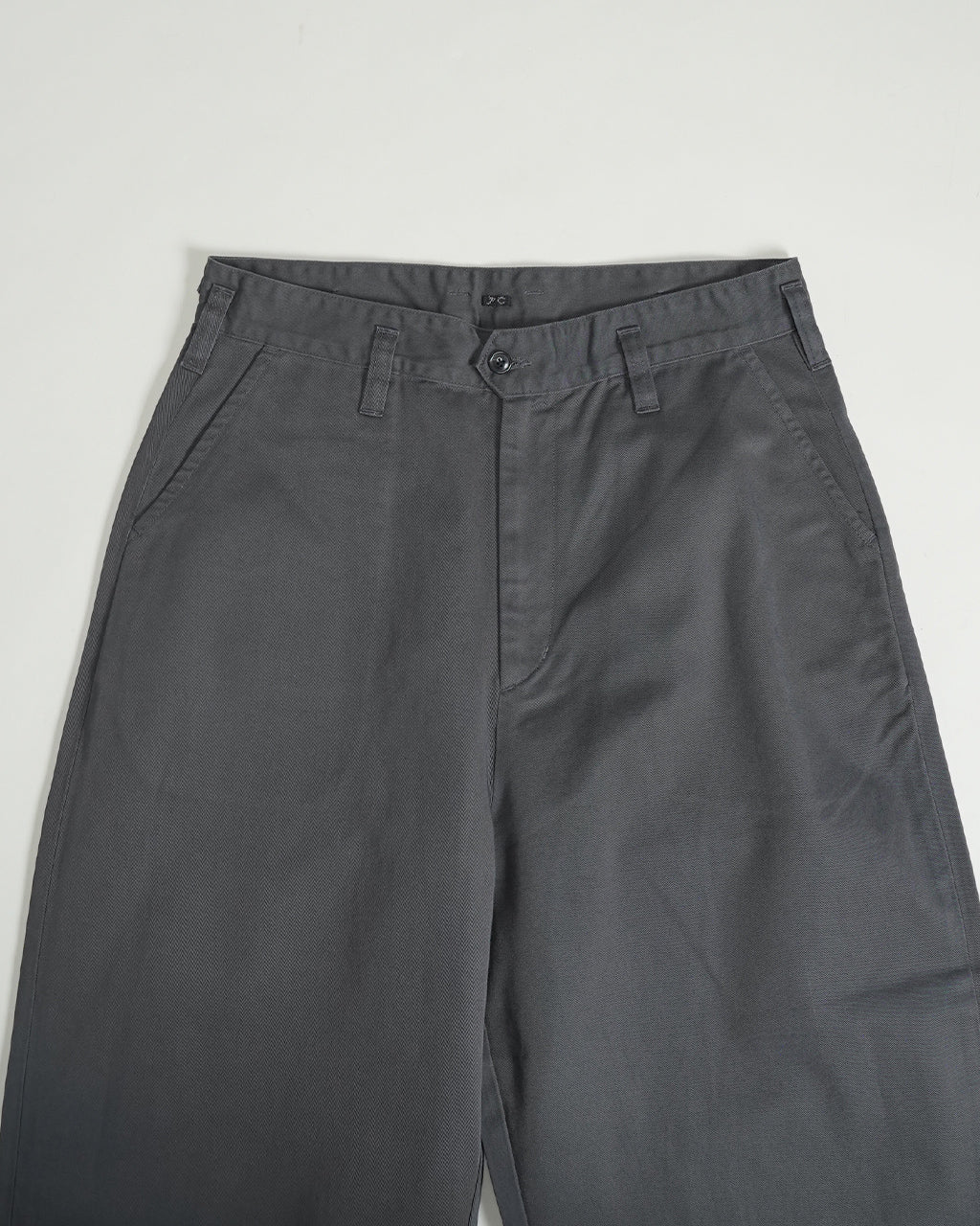 PORTER CLASSICのGENE KELLY CHINOSの前身頃を映す濃いグレー系パンツ。ウエスト周りのベルトループと前閉じ、股上のラインが見える。