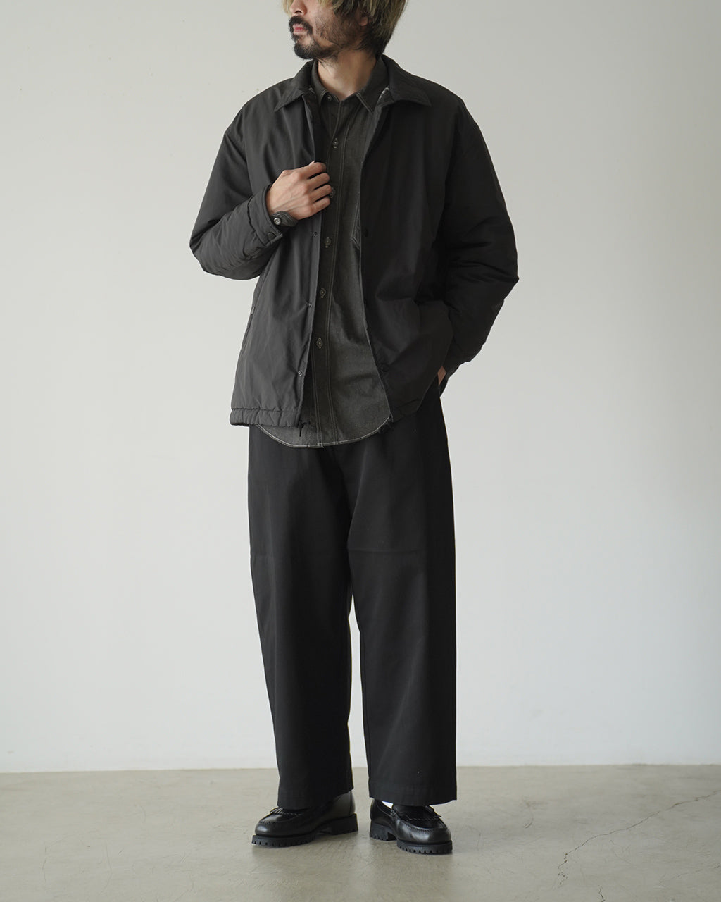 PORTER CLASSICの WEATHER COACH JACKETを着た男性の全身ショット。黒系のコーチジャケットとパンツを組み合わせた落ち着いたコーディネート。裾に絞りがあるデザインが特徴。