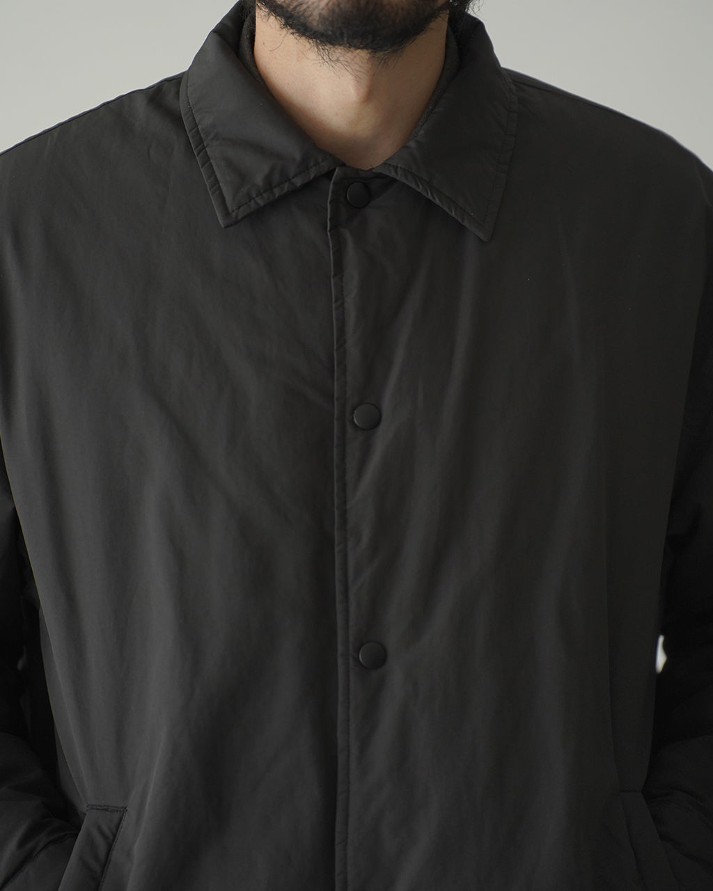 腰まで覆うブラックの Weather Coach Jacket の正面アップ。シンプルなスナップボタンとコットンライニングがのぞく、落ち着いた印象のジャケットです。