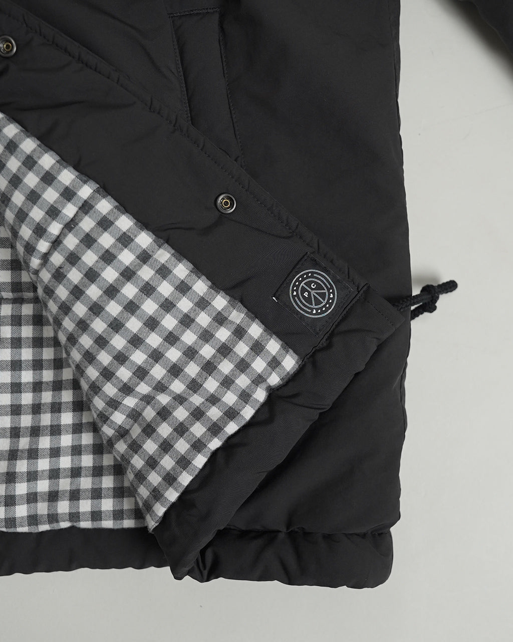 黒地のWeather Coach Jacketの裾と袖口のアップ。チェック柄の裏地が見える部分とボタン、ブランドタグのディテールが確認できる写真