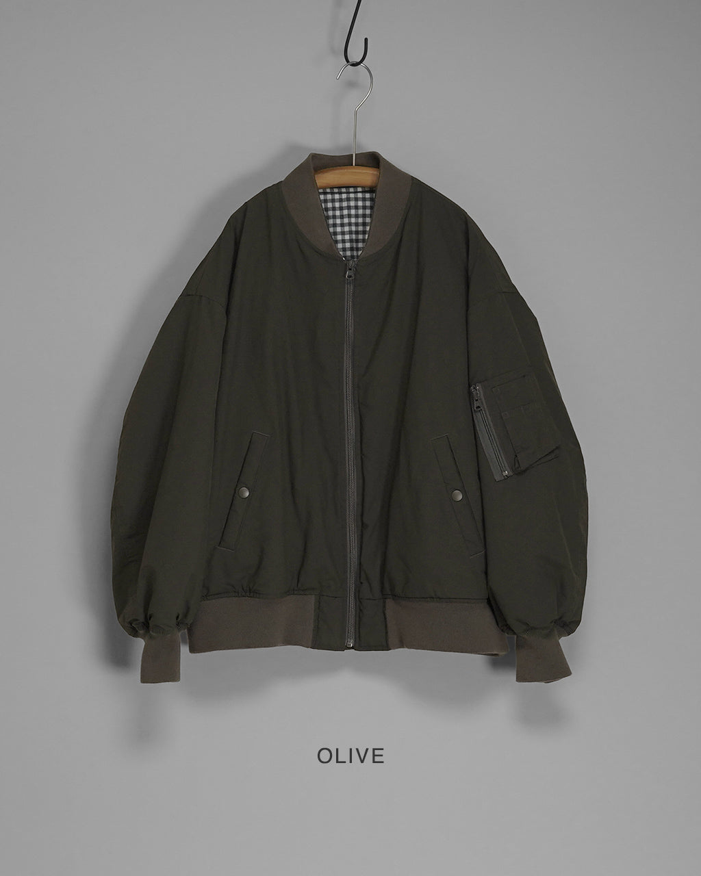 Olive系の中綿入りフライトジャケット。前面はジップ開閉、両脇にはスライドポケット、右腕にはファスナー付きポケットを配置したボリューム感のあるシルエット。裏地はチェック柄、リブ付き裾と袖口がカジュアルな雰囲気。