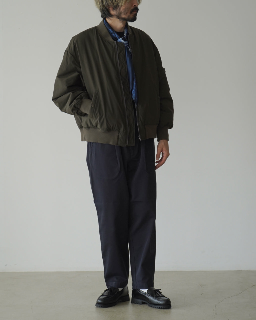 オリーブ色のWEATHER FLIGHT JACKETを着用した男性が正面から立つ様子。ゆったりとしたシルエットとリブ付きの裾・袖口が特徴的。ジップ開閉とポケットのディテールが見える全身写真。