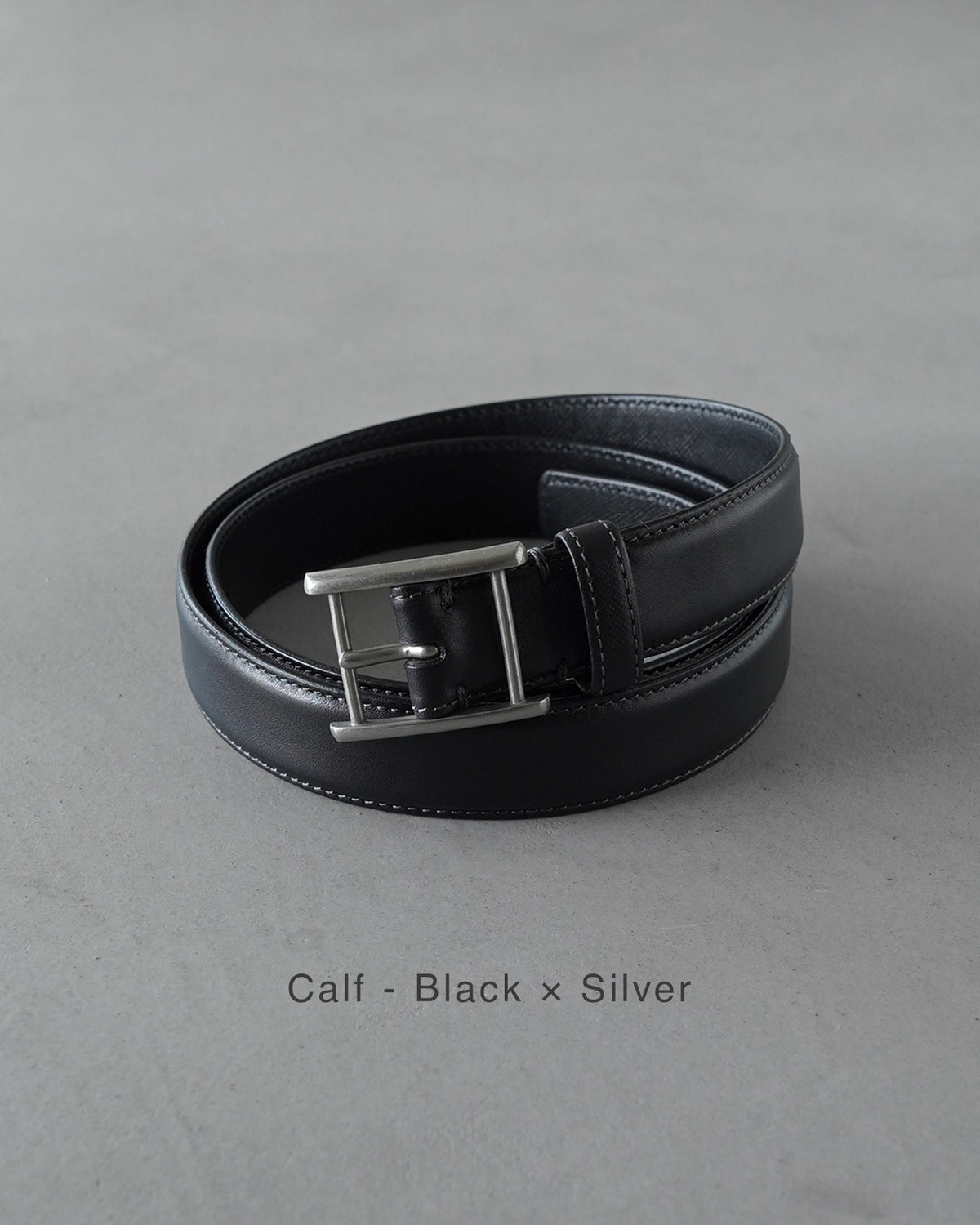 ブラック×シルバーのベルト。斜めから見えるバックルと、幅広めのレザーが際立つ、上品で控えめな印象のディテール写真。
