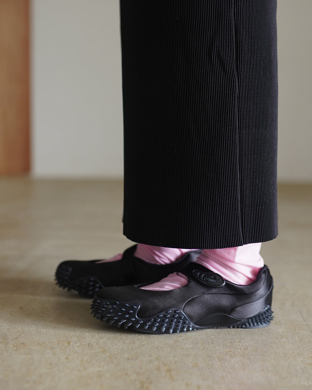 黒いスカートに合わせてPUMA Mostro Fey Satinを履いた横からの足元。低めのシルエットとスパイクソールが分かる