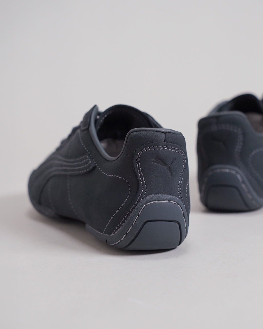 PUMAの黒系スニーカーの後ろ姿。丸みを帯びたヒールと白いステッチが目立ち、ソールは濃いグレー。ブランドのパッチ風ステッチも見える