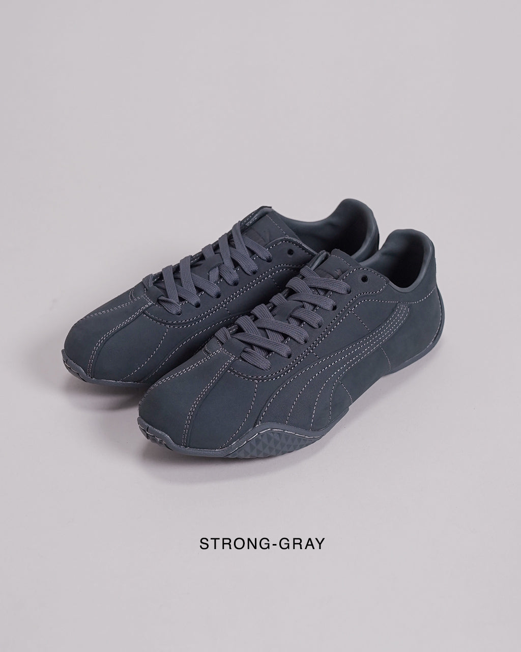グレー系のPUMAスニーカー、鋭いコントラストの白ステッチが特徴的。つま先から踵まで一体感のあるデザインで、サイドに沿う縫い目が目立つレースアップシューズ