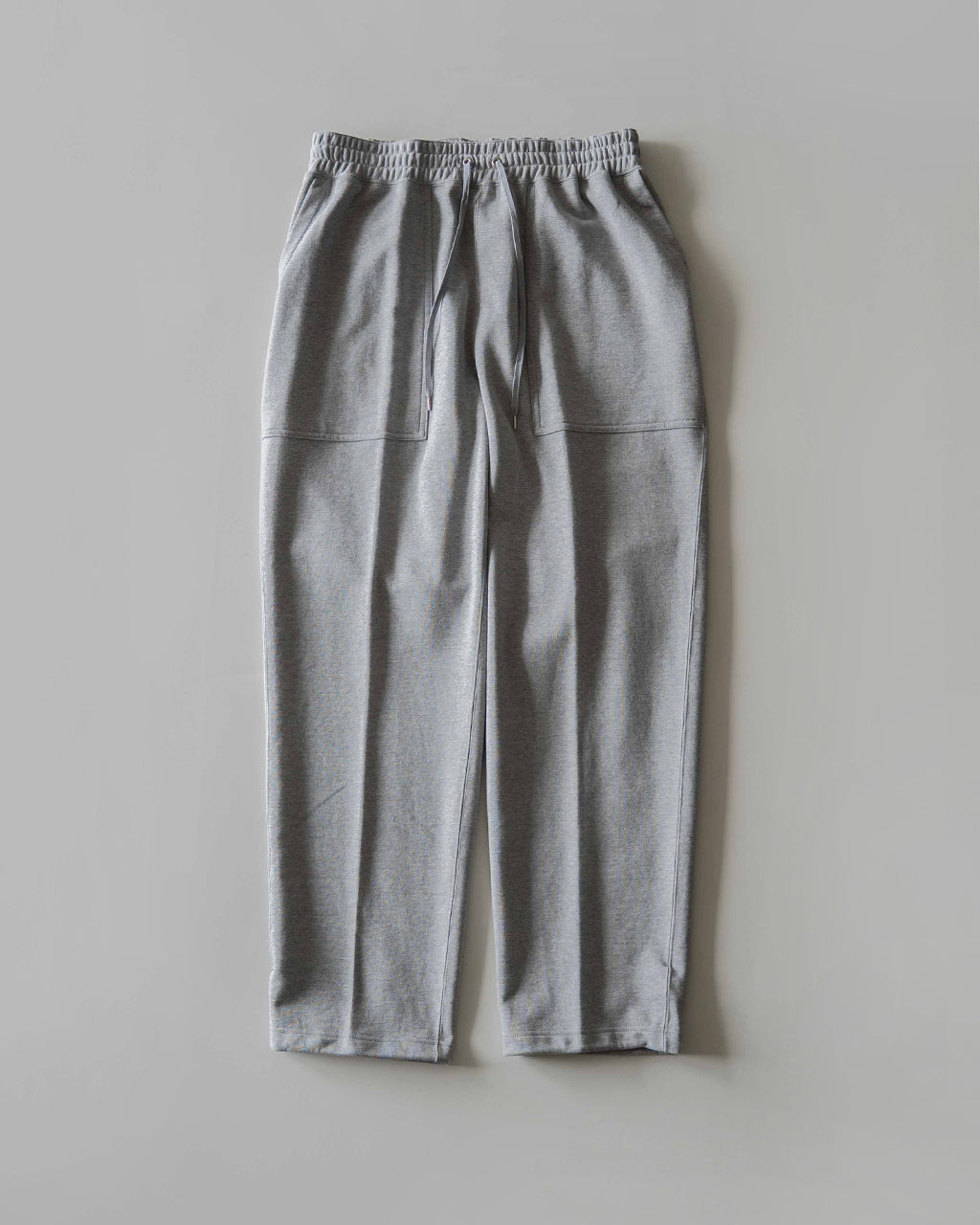 グレーの裏毛素材のスウェットパンツ。腰からヒップにかけてゆとりがあり、裾へ向かって緩やかにテーパード。前左右には大きなポケットを配置したデザイン。