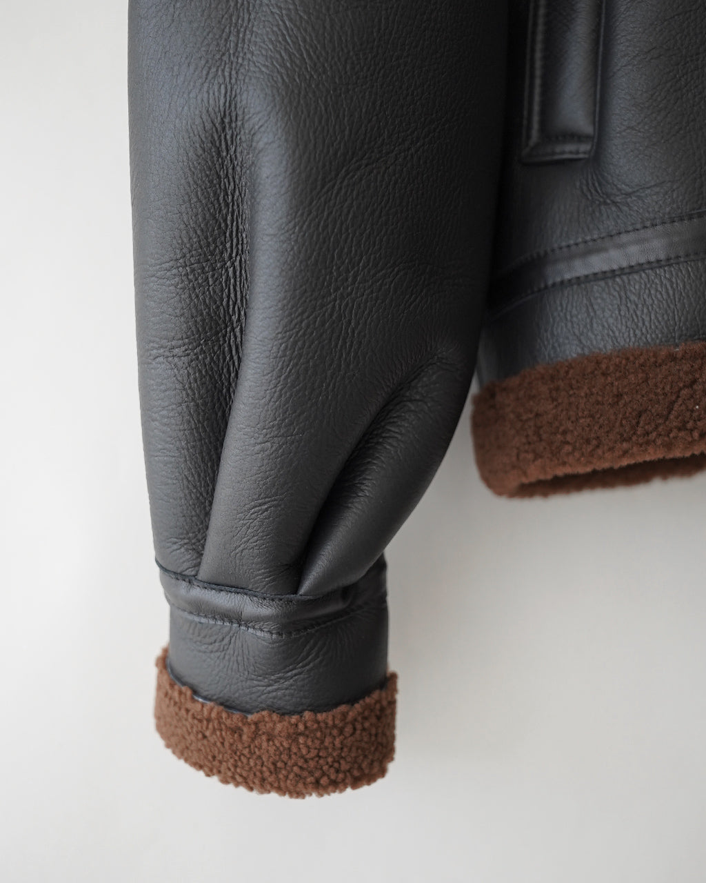 黒のレザー素材が美しいPLEATED AVIATOR JACKETの袖元アップ。裾は茶色のボア風パイピングで暖かみのあるディテールが見える