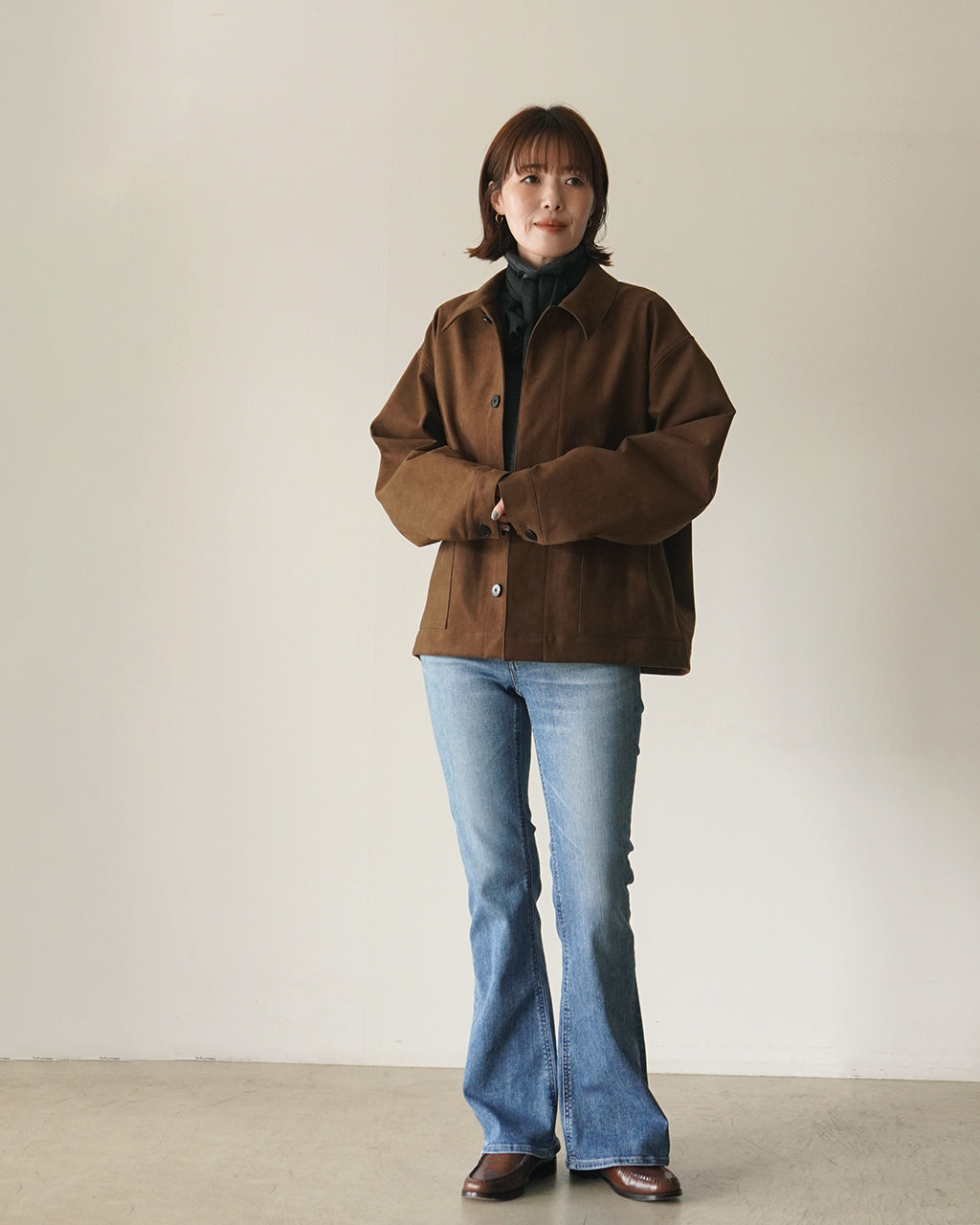 ブラウンのジャケットを着た女性が正面を向き、ワイドな袖とゆったりシルエットが強調されたコーディネートの全身像。