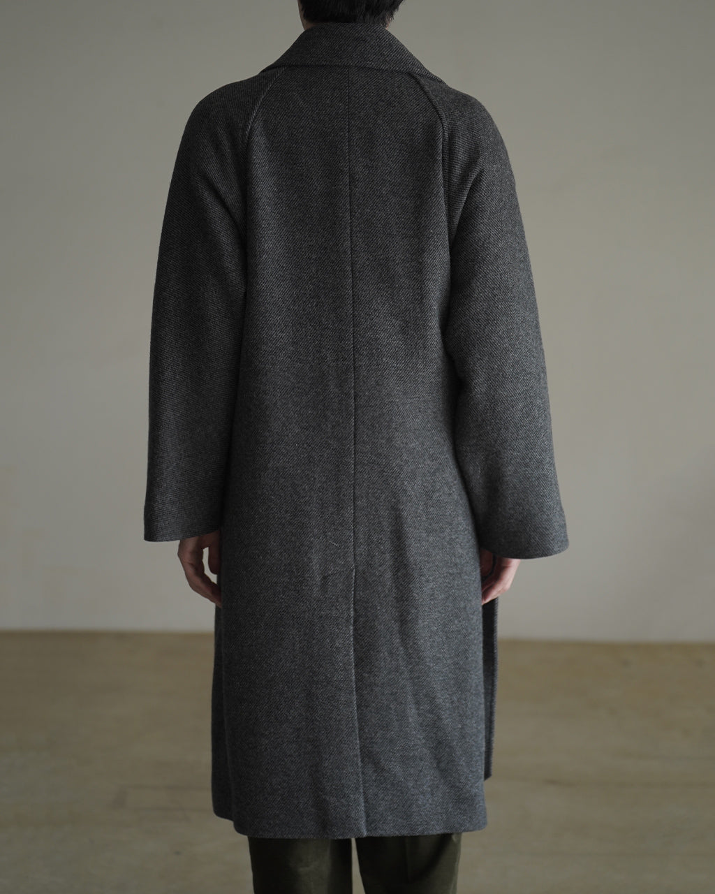 背中側から見るWRAP COAT RM262-034。深いグレーのウール混紡生地で、ゆったりとしたAラインのシルエットと長めの着丈が特徴的な一枚です。