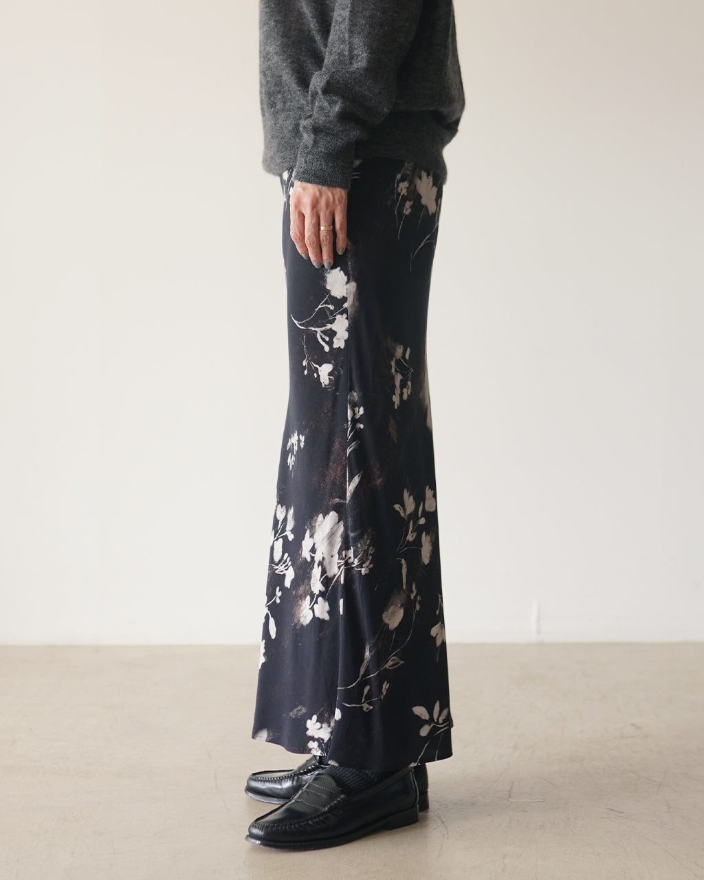 黒地に淡い花柄が散らばるロングスカート。横からみると細身のナローラインと裾の花柄が鮮明に見える着用イメージ。