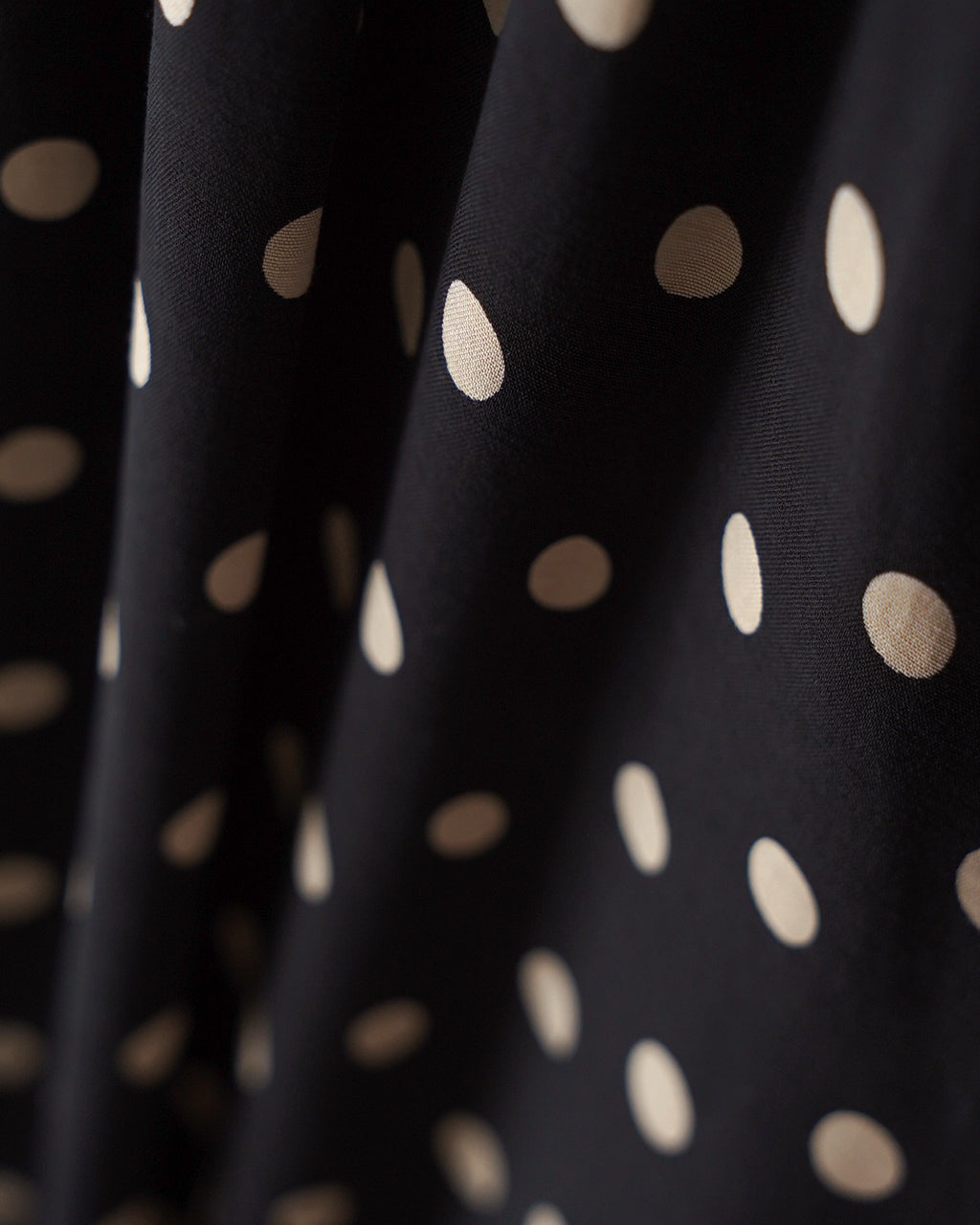 黒地に白いドットが散らばるPOLKA DOT'S OPの生地アップ。光沢のある滑らかな布地がドット柄を引き立て、しなやかな落ち感が伝わるショット。
