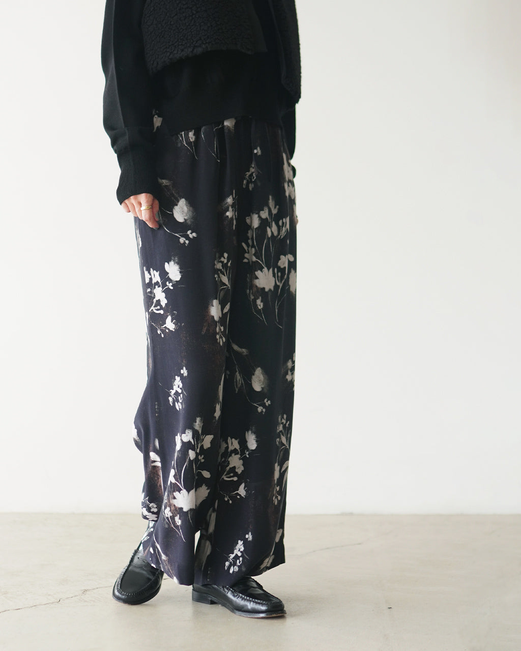 ブラックをベースに花柄プリントがのったSACRAのパンツ。全体は長めのワイドシルエットで、腰まわりはリラックス感のあるゴム仕様、裾に向かって緩やかに広がるラインが特徴。
