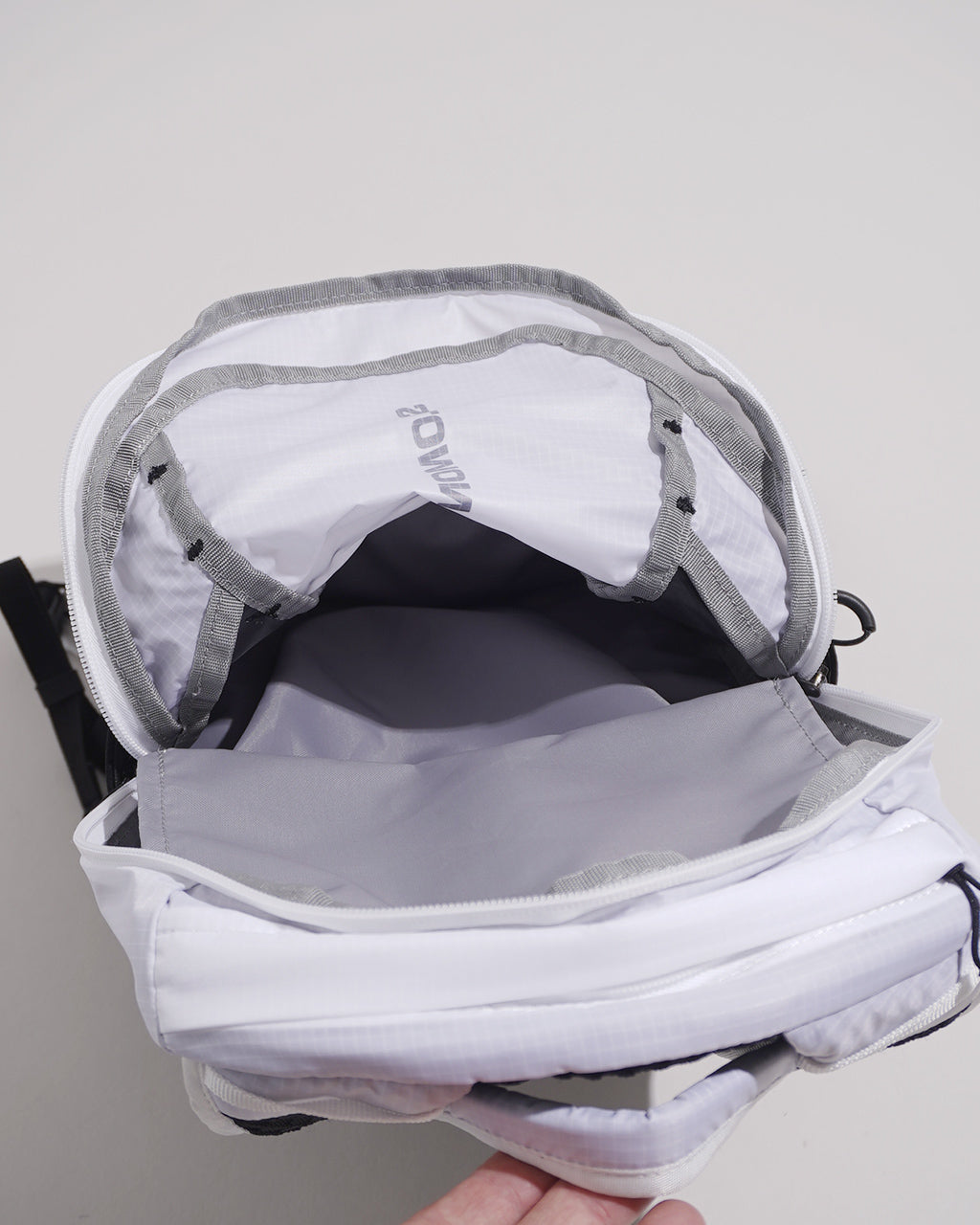 黒と白の対比が印象的なXT10バックパックの開口部を見せた内部ショット。内部収納とパッド入り背面の設計が確認でき、前後のグレーのストラップが配置されている。