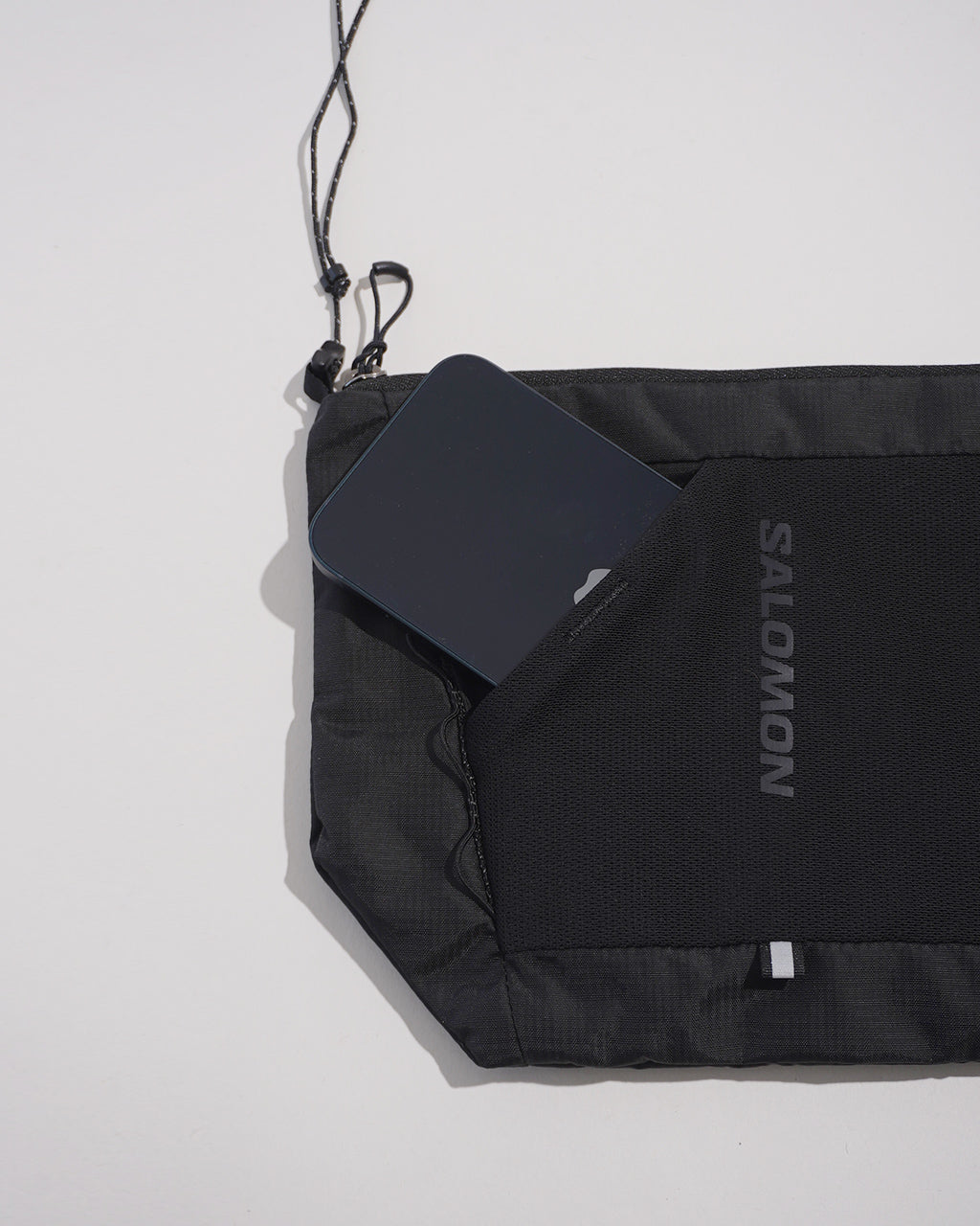 ブラック系のショルダーバッグの横からの様子。前面ポケットにSalomonのロゴとスマートフォンが挿入されているのが見える。