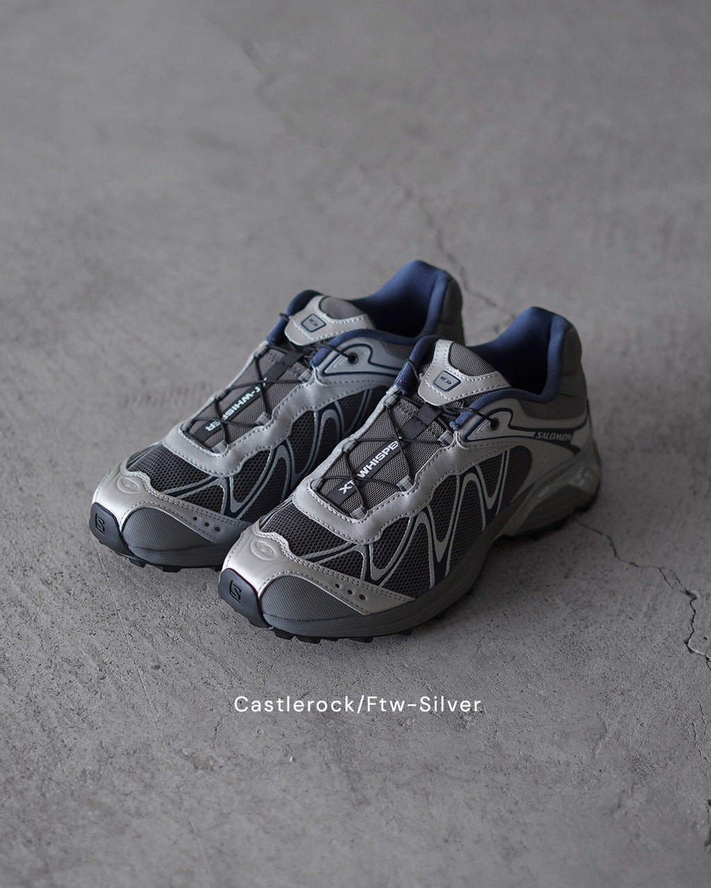 SALOMONのXT-WHISPER系スニーカー、グレー×ネイビーのメッシュとレザー風素材の組み合わせ。立体的なパネルと柔らかなカーブのソールが特徴的な前後ショット。