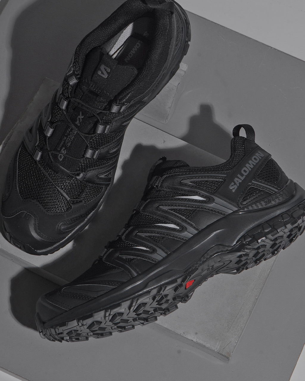 SALOMONのブラック系トレイルスニーカー、横から見た側面とつま先周りの丈夫そうなアウトソールを強調したデザイン。
