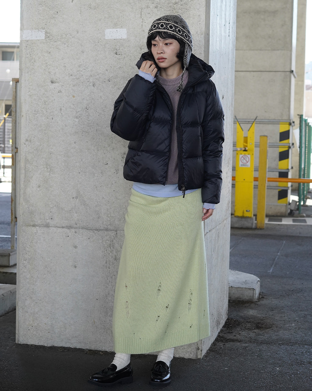 黒と白系の柄入りニットキャップ。幾何柄の編み模様が特徴で、耳元の紐部が垂れ下がるスタイルを演出している。