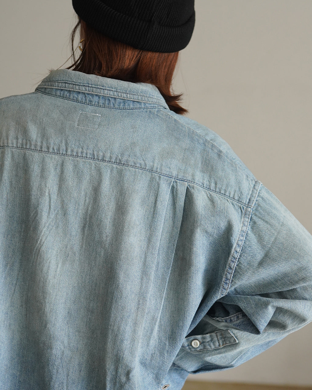 デニムシャツの後ろ姿。淡いブルー系のUSED風加工で、襟のラインと背中心の縫い目が目立つ。肩幅がゆったりと感じられるオーバーサイズのシルエット。