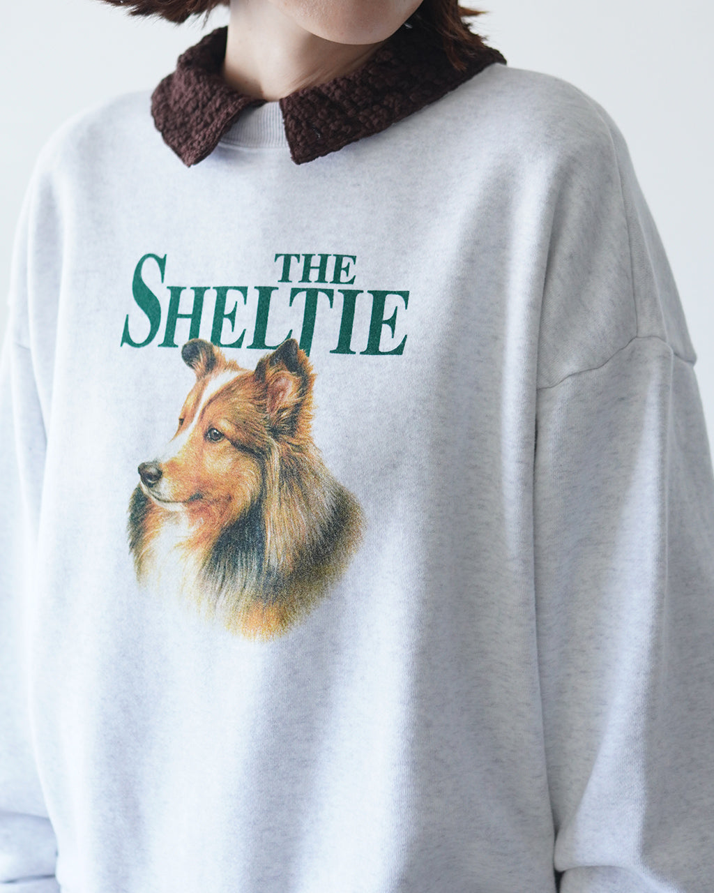 ヘザーグレーのTHE SHELTIE SWEATSHIRTに犬の横顔プリント。胸元付近のブランドロゴと犬モチーフが目を引くデザイン。