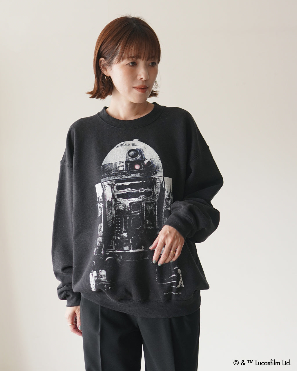 モデルが黒のR2-D2プリントスウェットを着用して横から視線を向ける写真。胸元にスターウォーズのR2-D2デザインが大きくプリントされ、リブ袖と裾のディテールが見える。