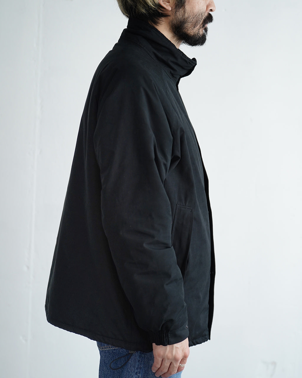 黒系のBaggies Jacket Ver.2を横から着用した男性のシルエット。高めの襟とすっきりとしたフロントデザイン、ややAラインの裾が特徴。細身のパンツとの組み合わせが映える端正な外観。