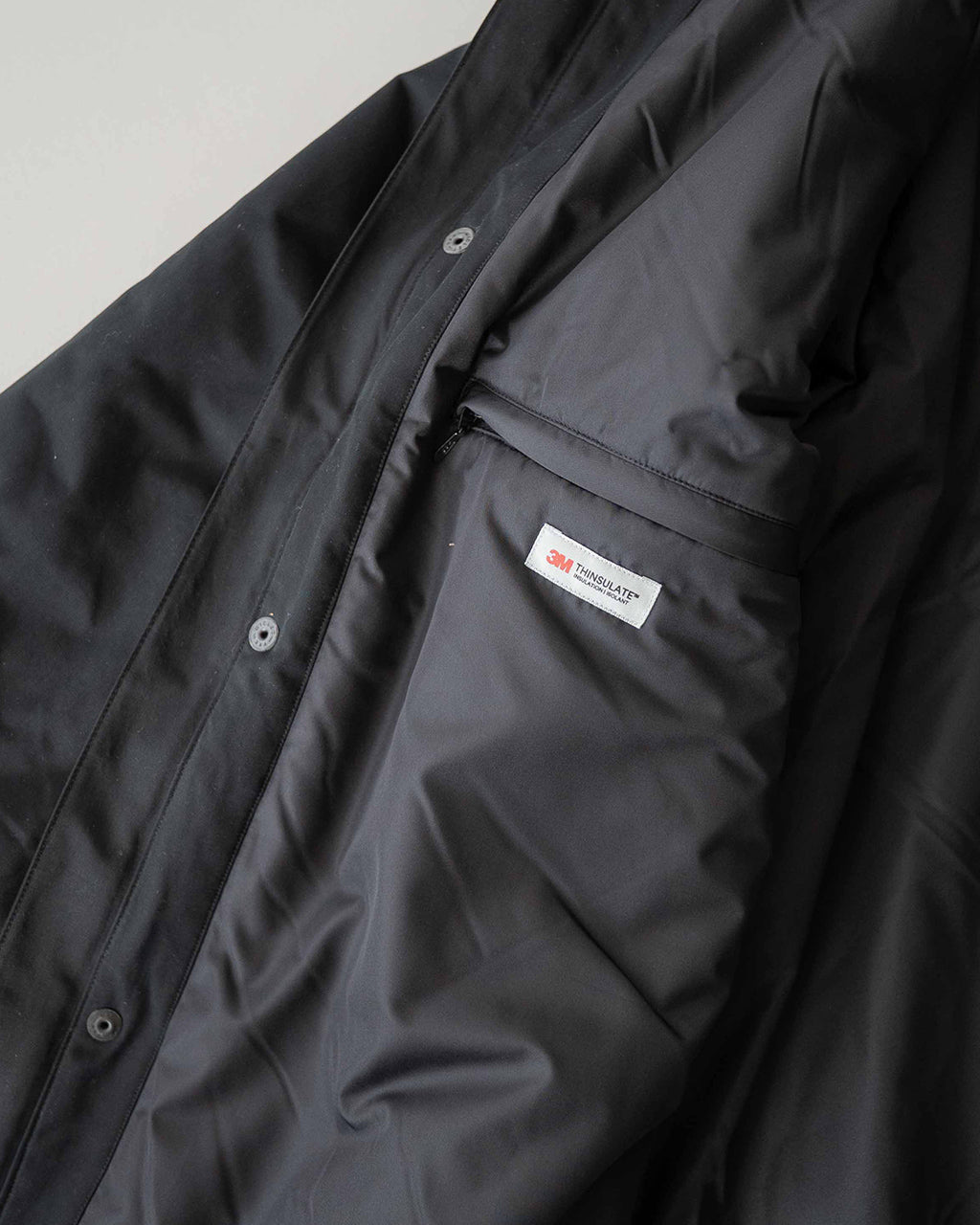 ブラック系のジャケット正面下部のポケット口と内ポケットの3M THINSULATEタグが見える着用イメージ