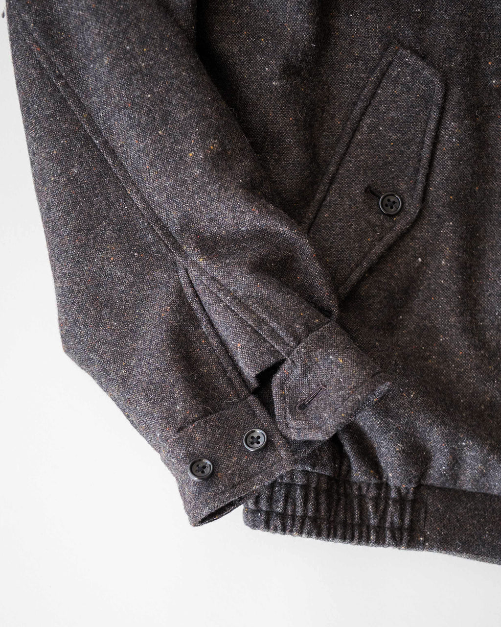 杢調のダークセピア系ウール混素材の Harrington ジャケット。袖口と裾のリブ、前立てポケットのディテールが見える横向きショット。