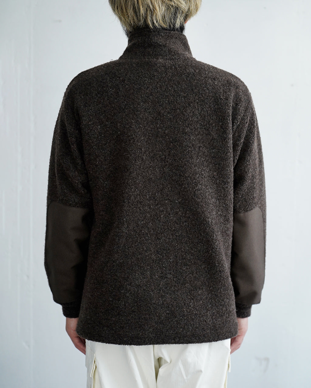 背面から撮影されたウールパイルハーフジップ pullover。ダークブラウンのボディに肘部分は別素材で切り替えられ、立ち上がりの高いスタンドカラーが特徴です。