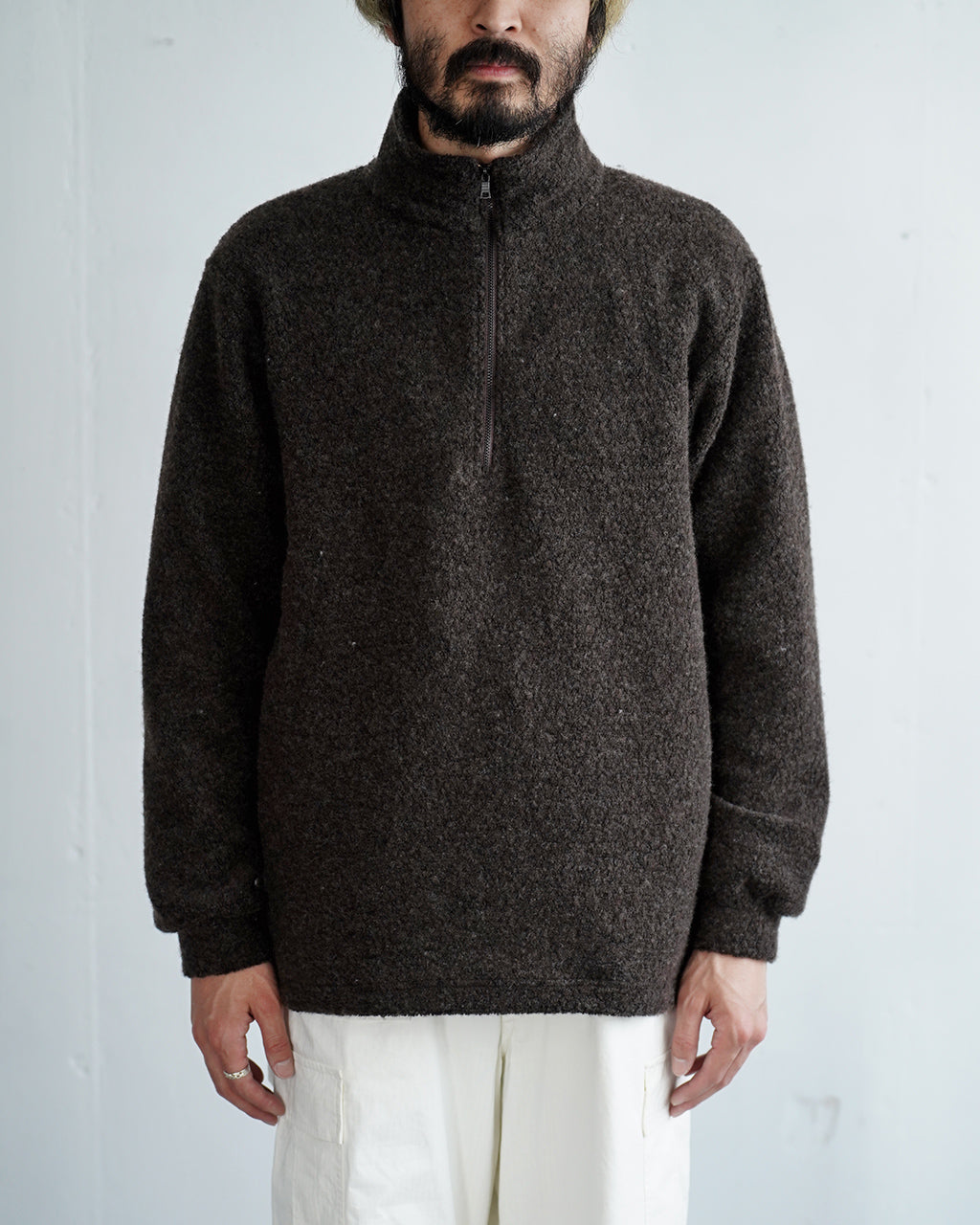 ダークブラウンの Wool Pile Half Zip Pulloverは、立ち襟とジップヘッドの特徴的なデザイン。ゆったりとしたシルエットで肩の力を抜いたカジュアルな着こなしが映える姿。