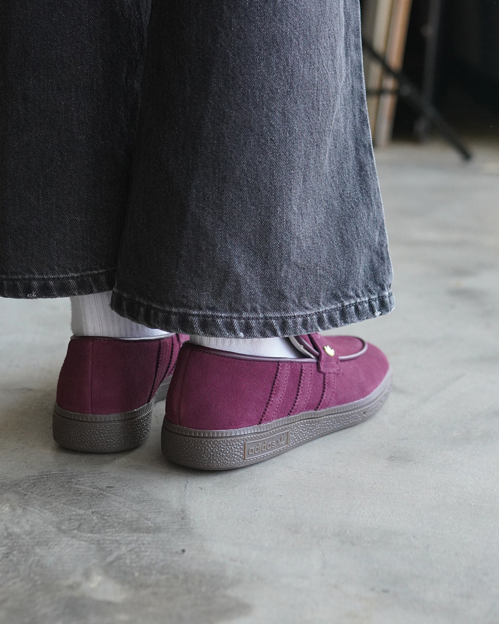 アディダス HANDBALL SPEZIAL LOAFER の後ろ姿。ダークデニム地のパンツを着用した人の足元が鮮やかなマルーン系のスエードローファーで見える