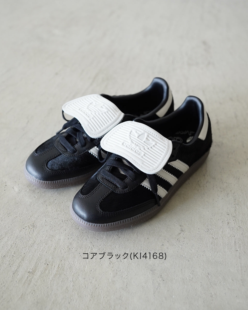 黒ベースのサンダル型スニーカー。白のマジックテープと三本ラインがアクセントになり、前方は丸みのあるシューズ形状、踵部分はやや細身でシャープな印象です。