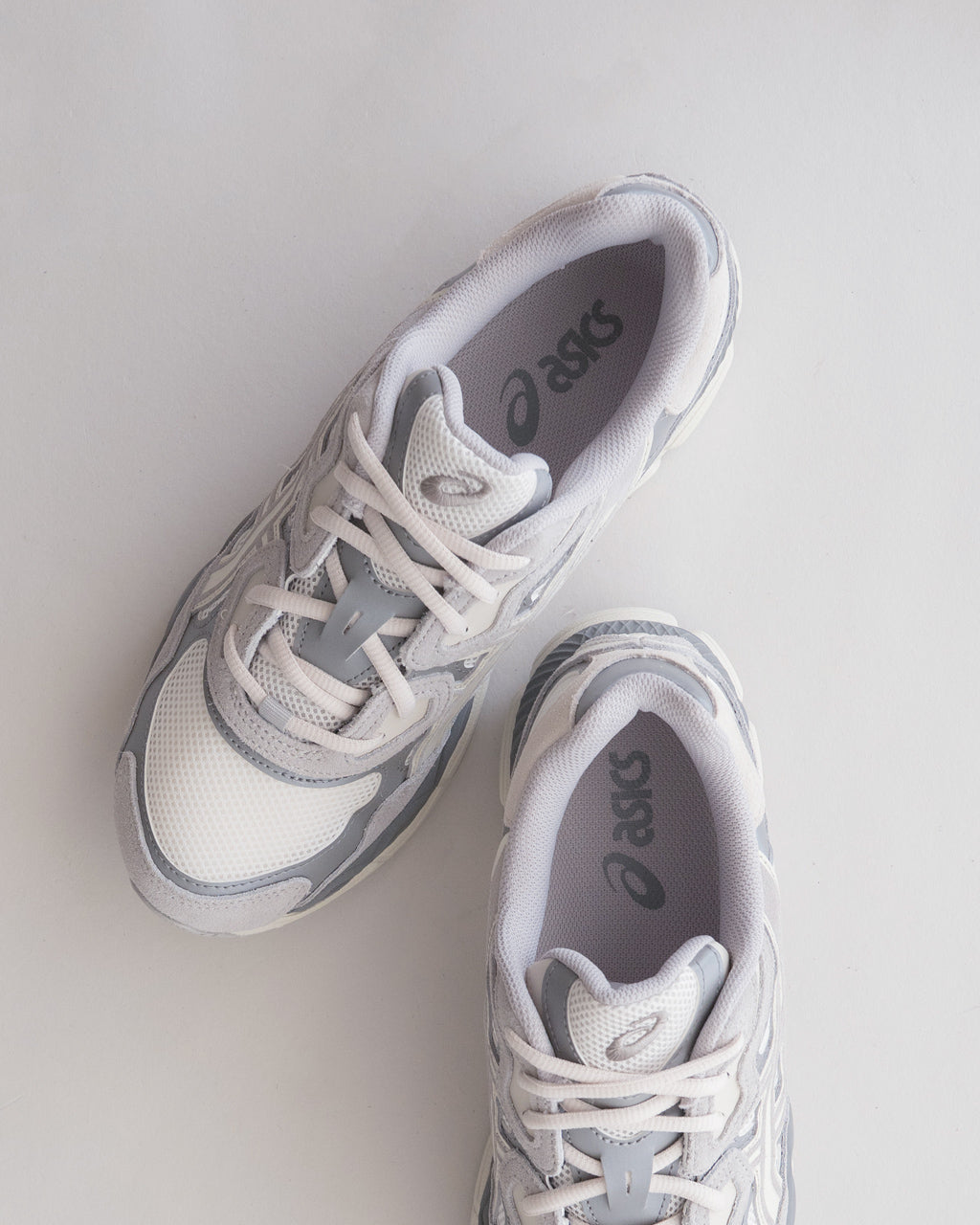 ASICSのスニーカー、白と淡いグレーの組み合わせ。つま先と側面のアップリム、メッシュ素材の通気性が見て取れる。