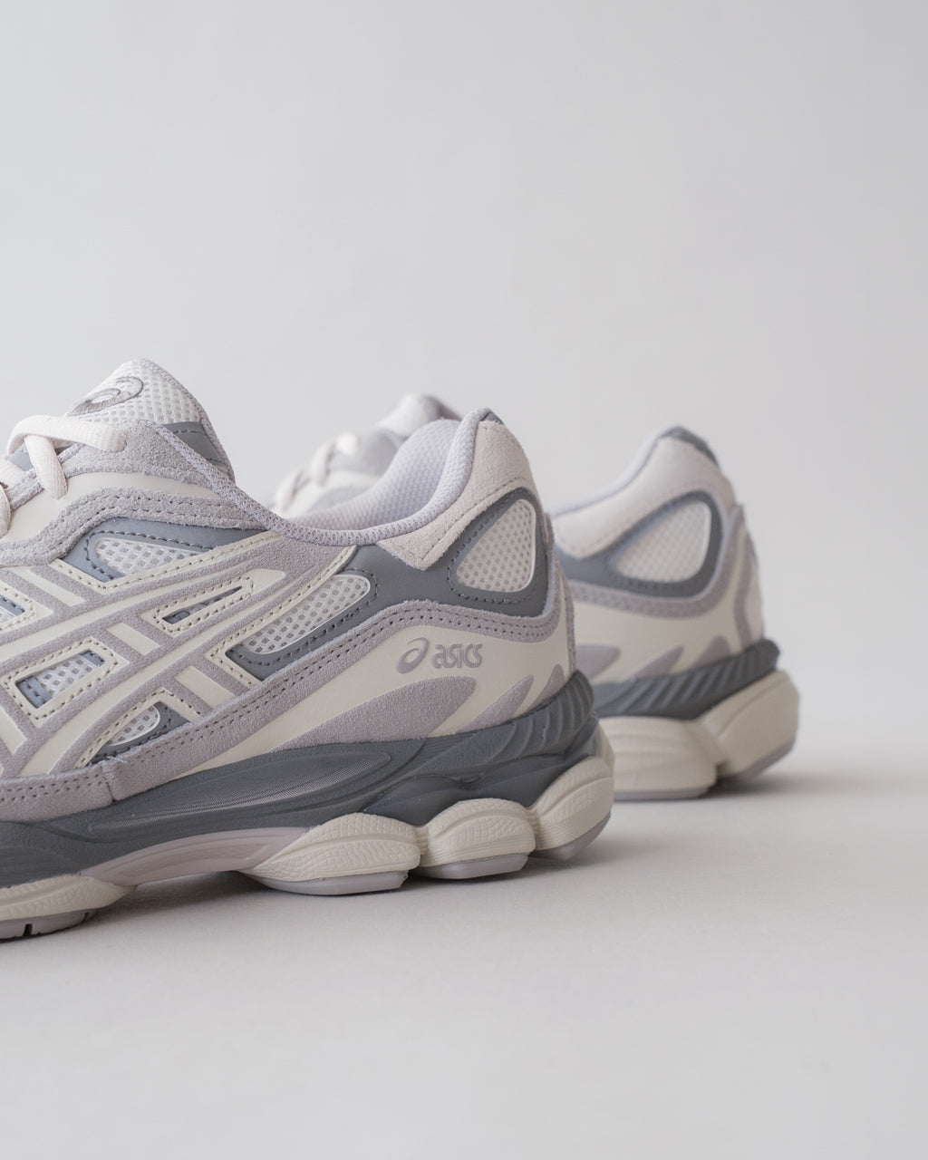 ASICSのグレー系スニーカー、前方と横から見える層状のソールと通気性メッシュを特徴としたデザインです。ブランドロゴが側面に控えめに配置されています。